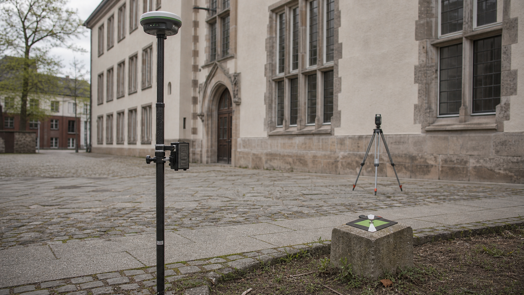 GNSS-Rover und Festpunktmarke vor einem Bestandsgebaeude